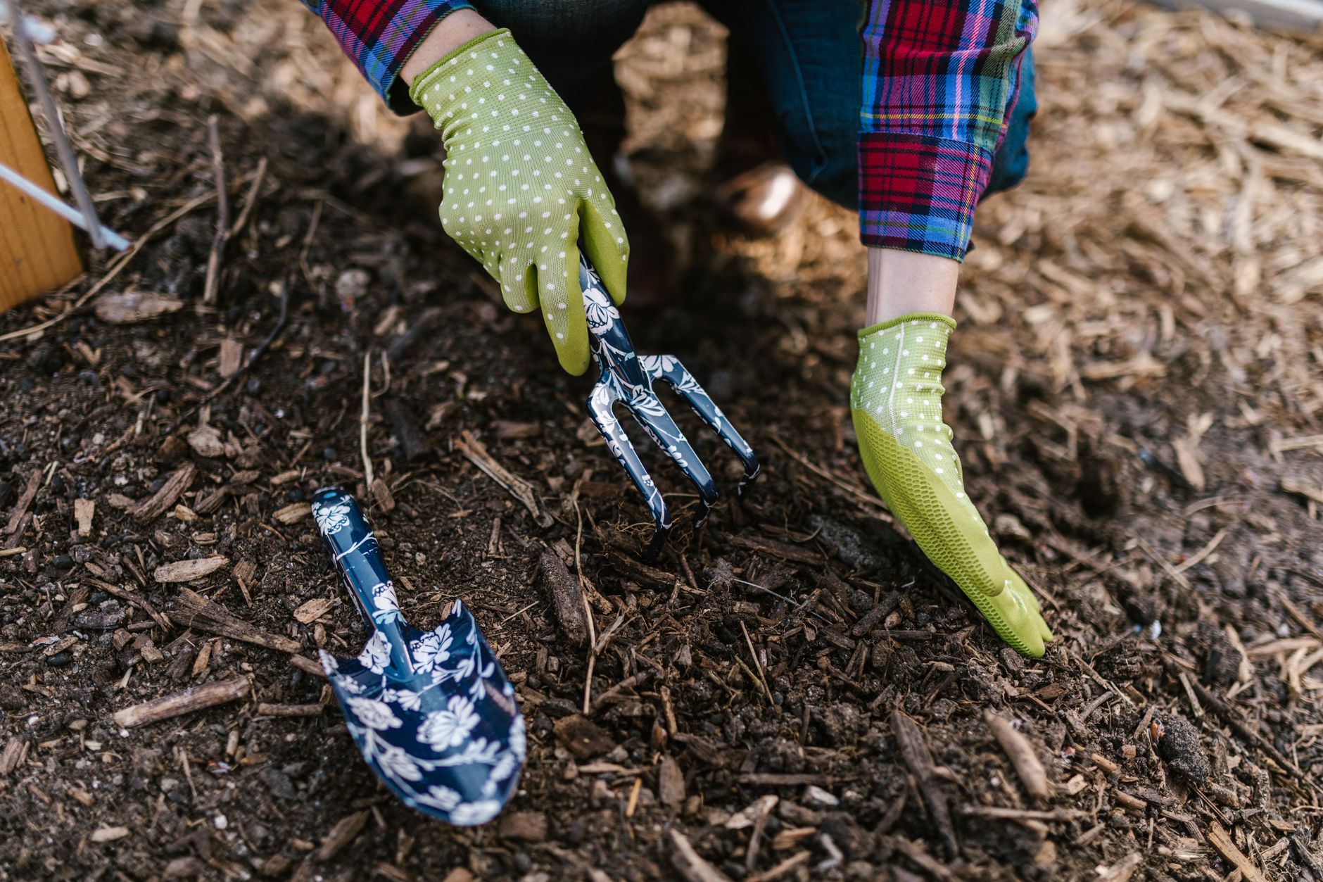 Person wearing gloves using garden tools to plant in soil