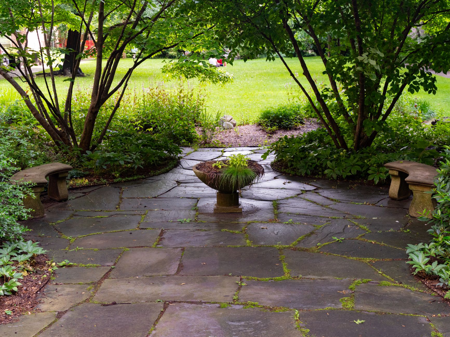 Peaceful stone patio surrounded by greenery and a central plant centerpiece in a garden