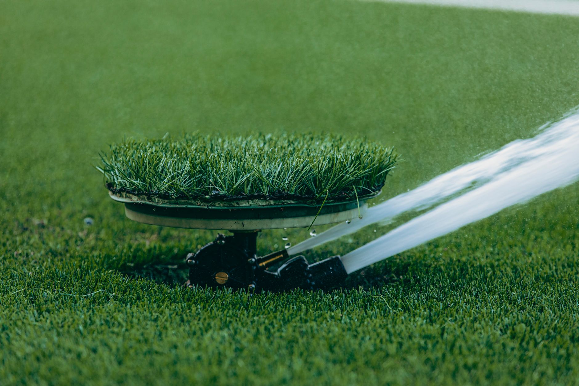 A close-up of an automated lawn sprinkler in action on lush grass